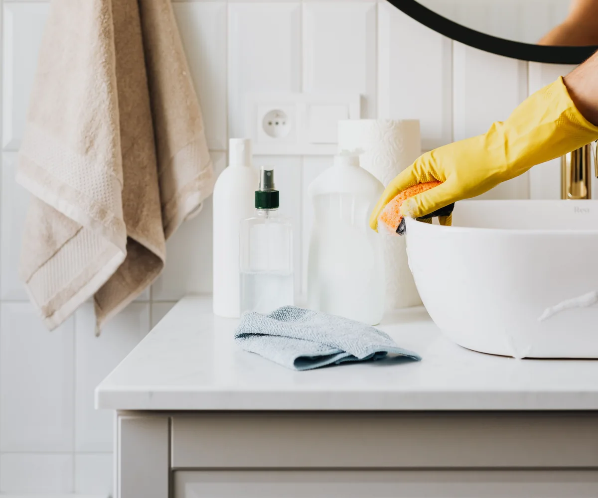 Stock photograph of yellow-gloved hands wiping a white bathroom sink
